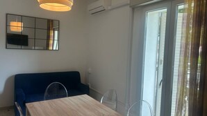 A room with a wooden dining table, a blue sofa, a large mirror, and a sliding glass door. - CV004 - Cervia, new three-room apartment with air conditioning (Cervia)