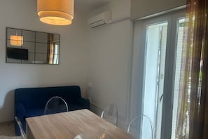 A room with a wooden dining table, a blue sofa, a large mirror, and a sliding glass door.