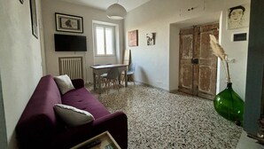 Ein Wohnzimmer mit einem violetten Sofa, einem Esstisch mit Stühlen, einem Fernseher und Bildern an den Wänden.