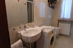 Casa de banho com lavatório, espelho, sanita e máquina de lavar roupa.