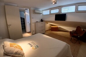 A bedroom with a bed, a desk, a chair, a wardrobe, and a TV on the wall.