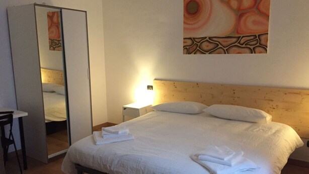Een hotelkamer met een bed, nachtkastje, stoel, spiegel en een schilderij aan de muur.
