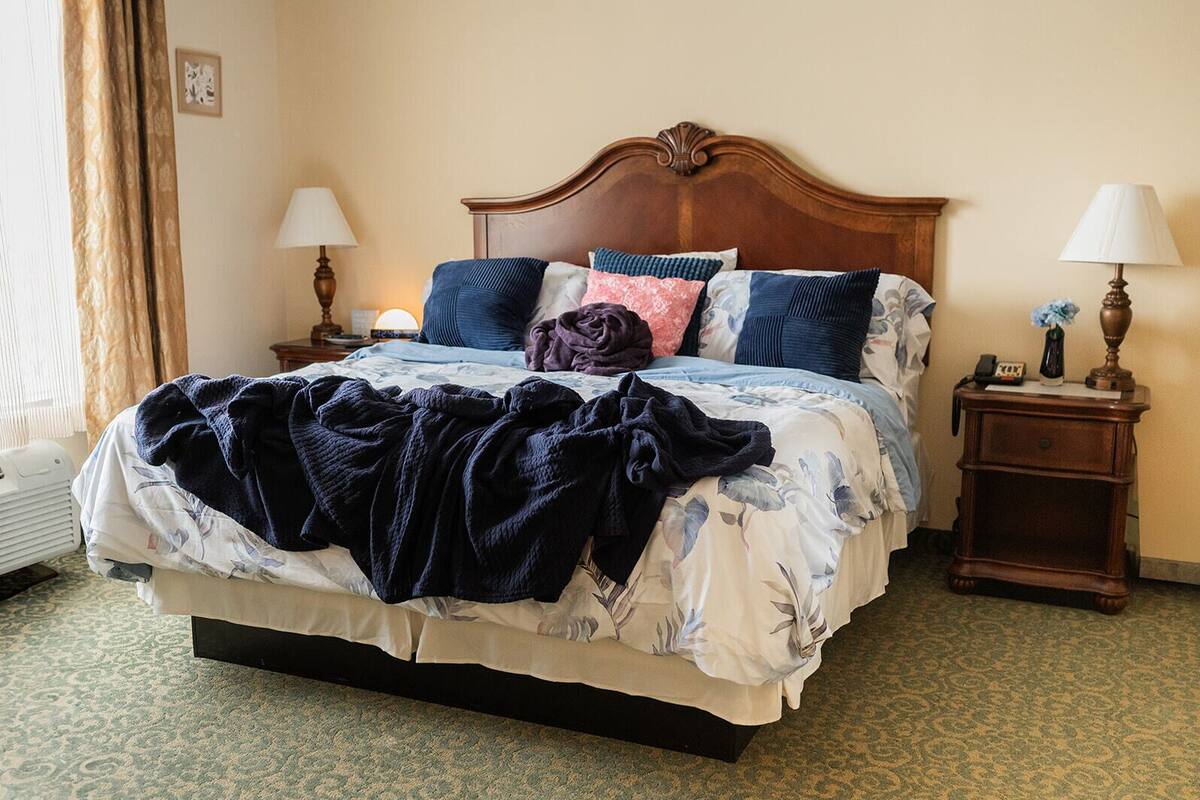 Una cama bien hecha con una colcha estampada, dos mesitas de noche con lámparas y un reloj de pared.