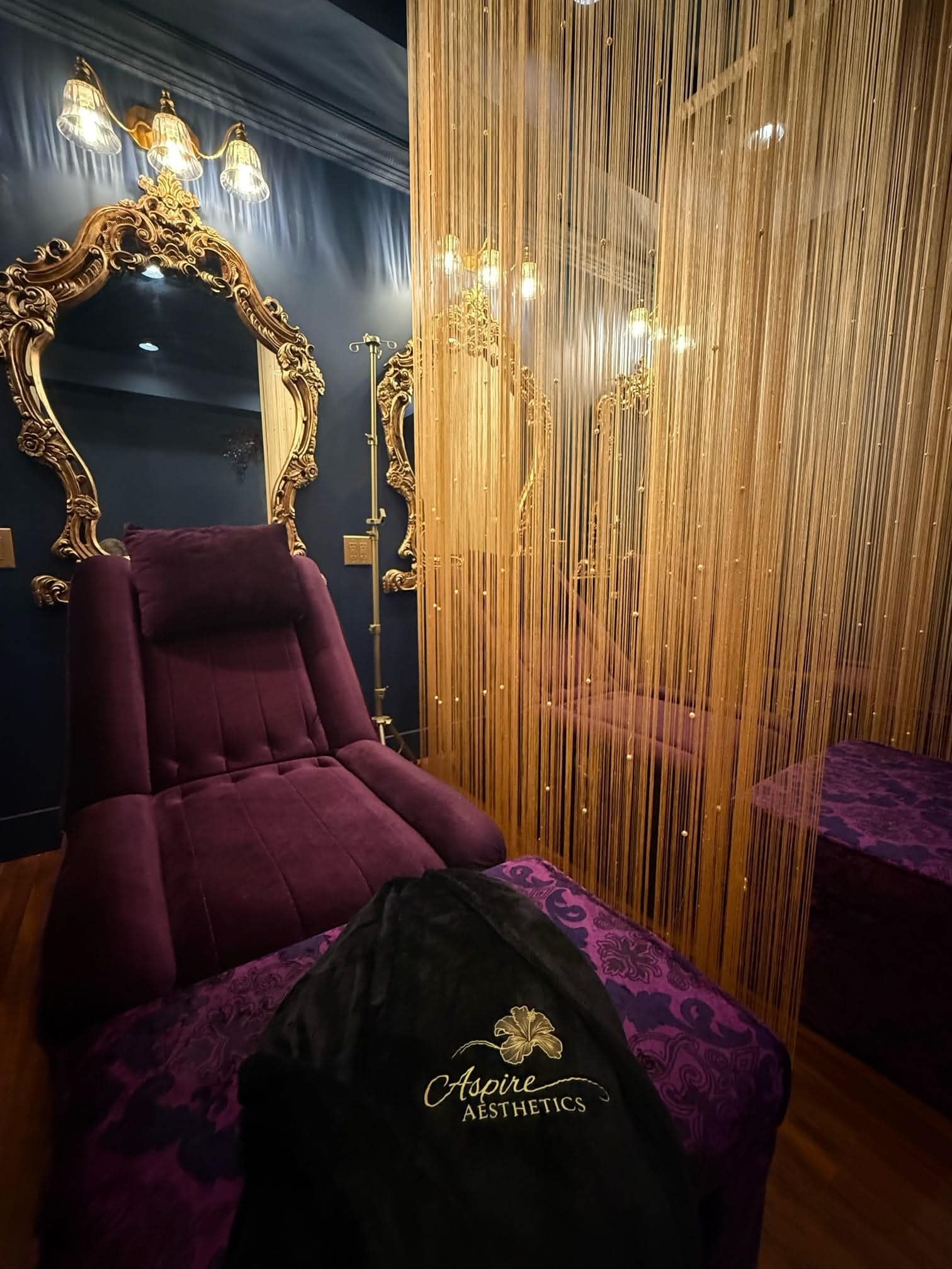 A room with a large ornate mirror, a purple armchair, and a decorative curtain.