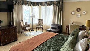 Un dormitorio con una cama grande, dos sillones, un sofá, un tocador, un televisor y una lámpara.