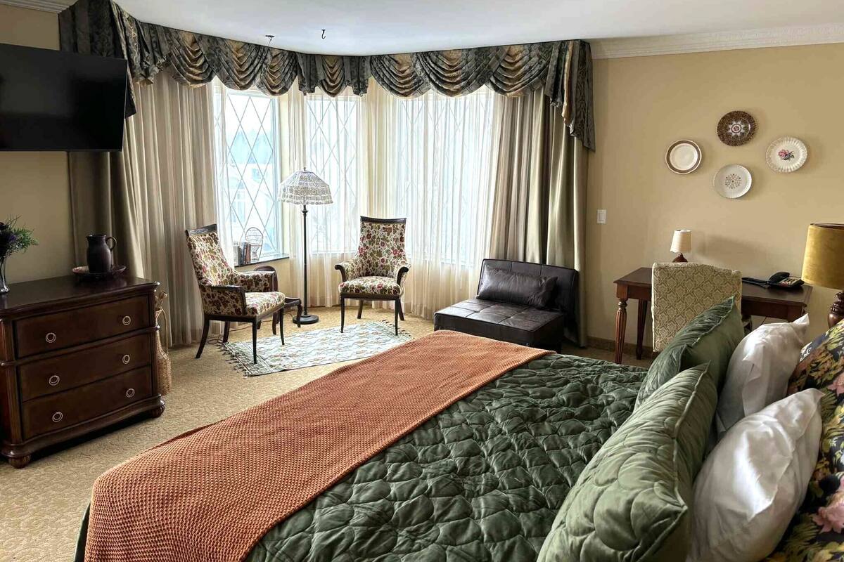 Un dormitorio con una cama grande, dos sillones, un sofá, un tocador, un televisor y una lámpara.
