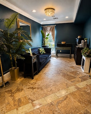 A living room with a dark blue wall, a black sofa, a large potted plant, and a chandelier. - Aspiratinns Hotel & Wellness Center (Slate Hill)