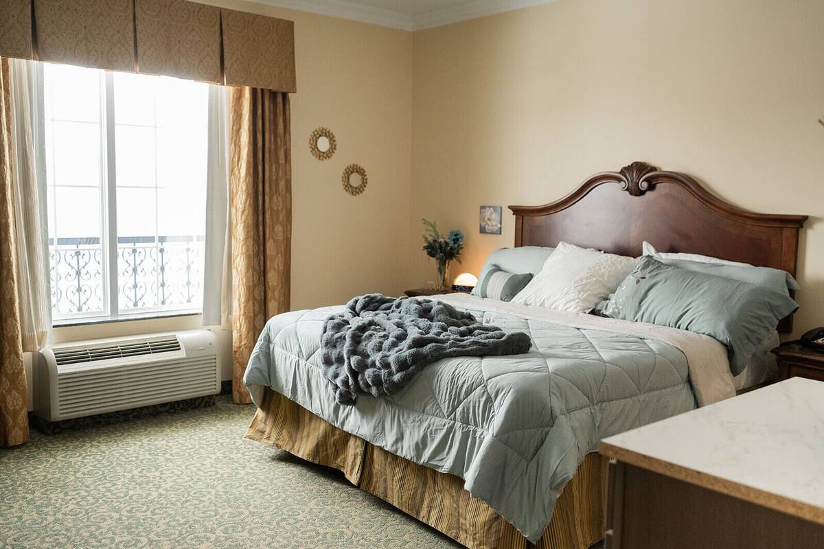 Una habitación de hotel con cama, mesita de noche, cortinas y un radiador.