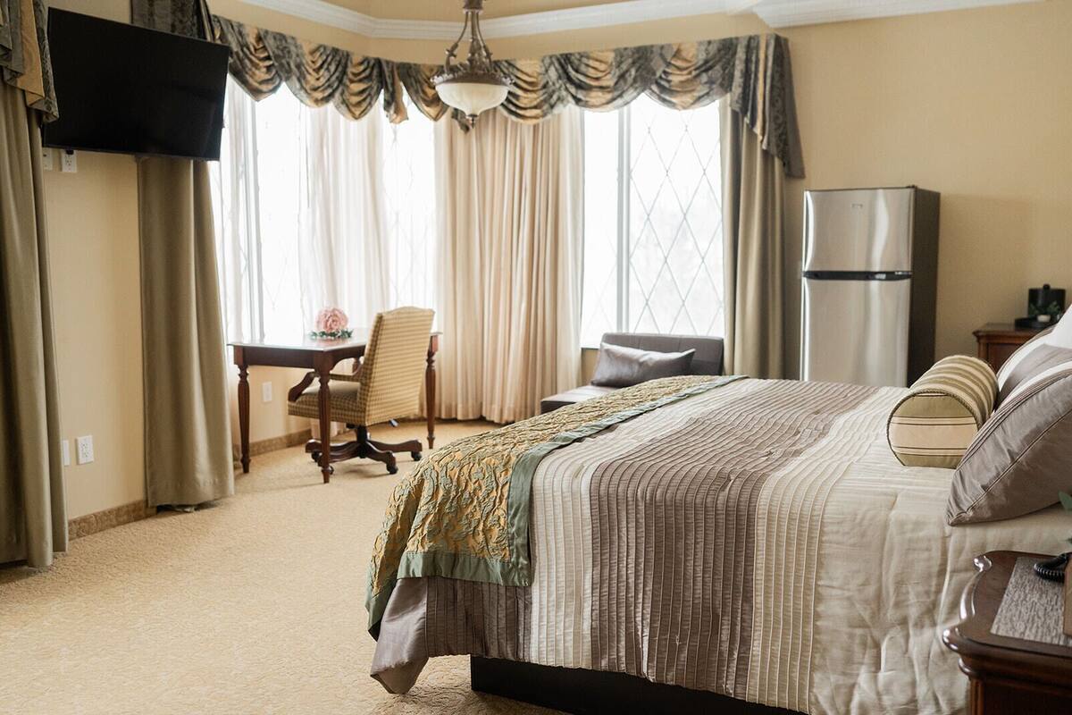 Una habitación de hotel con una cama grande, un escritorio, una silla, un televisor y un refrigerador.