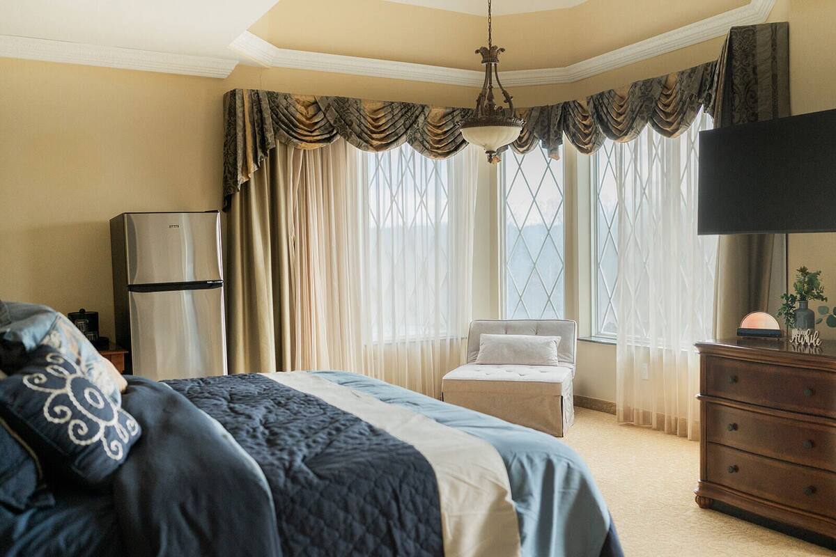 Una habitación de hotel con cama, cómoda, televisor y ventana con cortinas.