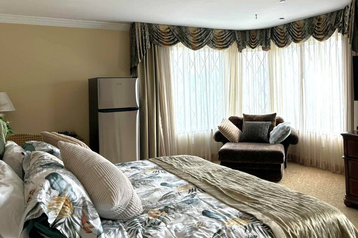 Una habitación de hotel con cama, una silla, cómoda, televisor y refrigerador.