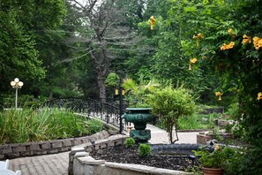 A garden with a curved metal fence, a stone pathway, and a green decorative urn.