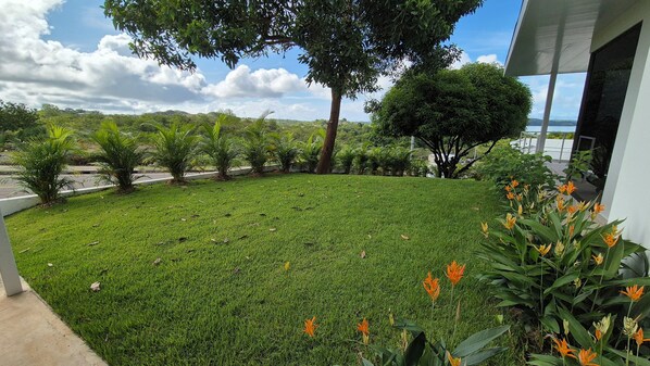 A well-maintained grassy area with a variety of plants and trees, a clear sky, and a distant view of hills.