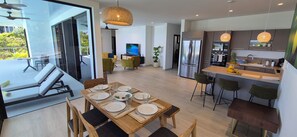 Eine moderne Küche mit einem großen Kühlschrank, eine Essecke mit einem Holztisch, gedeckt für sechs Personen, und ein Balkon mit einer Sitzecke.