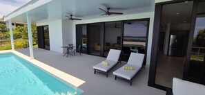 Ein moderner Außenpoolbereich mit zwei Liegestühlen, einem Tisch und Deckenventilatoren.