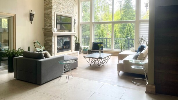 A spacious living room with a fireplace, large windows, and modern furniture. - Spacious Retreat in the Pines • Walk to Georgian Bay Beaches (Tiny)