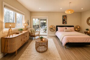 Une chambre à coucher comprenant un lit, des tables de chevet, une commode, une chaise, une petite table ronde en osier et une grande fenêtre.