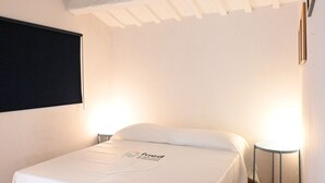 Un lit simple avec une couvre-lit blanche, une petite table de chevet et un téléviseur fixé au mur.