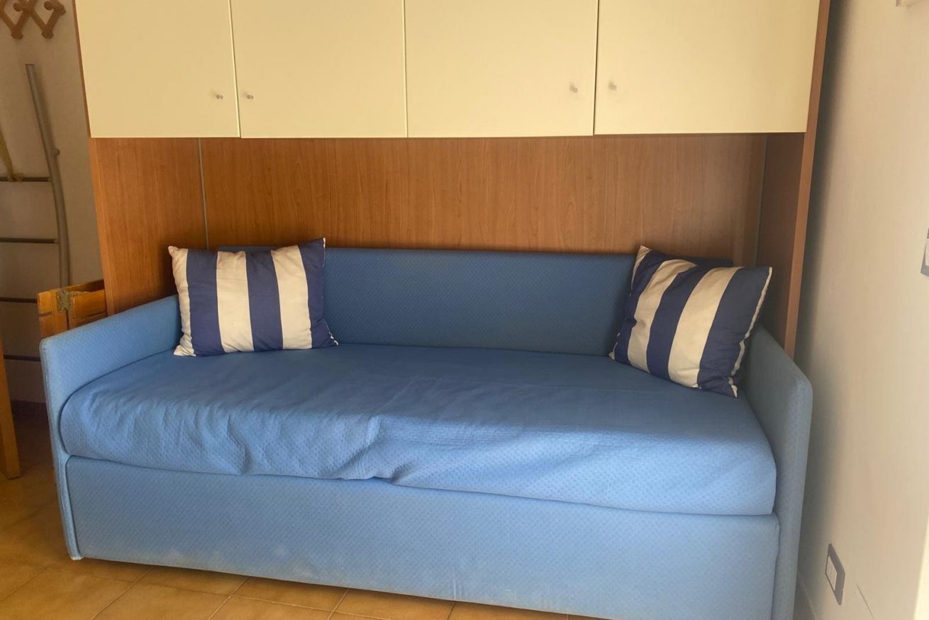 A blue sofa with striped pillows, a wooden headboard, and white cabinets above.
