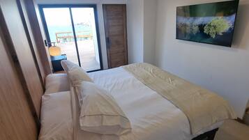 Un dormitorio con cama, televisor en la pared y vista al mar a través de un ventanal corredero.