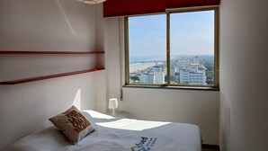 A hotel room with a bed, a window with a city view, a red ceiling, and a white lamp. - CV011 - Milano Marittima, sea front three-room apartment with exclusive view (Cervia)