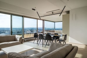 A modern living room with a large window, a dining area, and a sofa.