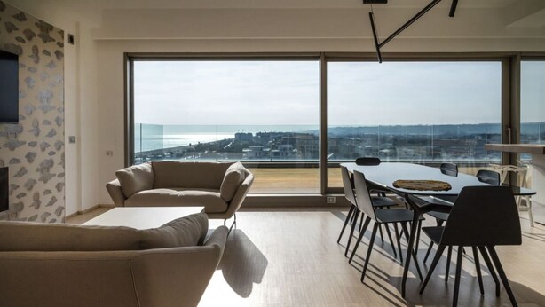 A modern living room with a large window, a dining area with a table and chairs, and a sofa. - Between sun and moon - Civitanova, noble apartment facing the sea (Civitanova Marche)