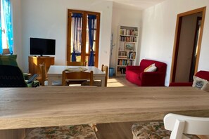 A living room with a wooden dining table, a red sofa, a bookshelf, and a television.