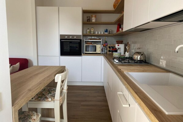 A compact kitchen with white cabinets, a wooden countertop, a built-in oven, a microwave, and a kettle.
