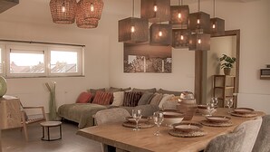 Un comedor con una mesa de madera dispuesta para cuatro personas, rodeada de sillas acolchadas. Un espejo grande refleja la habitación, y una ventana ofrece vistas de la ciudad.