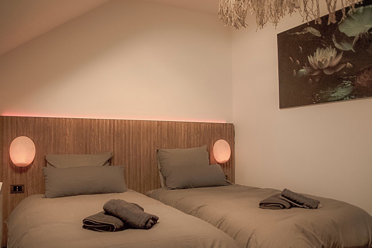Une chambre avec deux lits, chacun doté d’une lampe ronde fixée au mur et d’un oreiller.