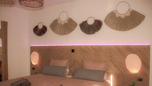 Un dormitorio moderno con cabecera de madera, dos mesitas de noche y una cama con almohadas y toallas dobladas.