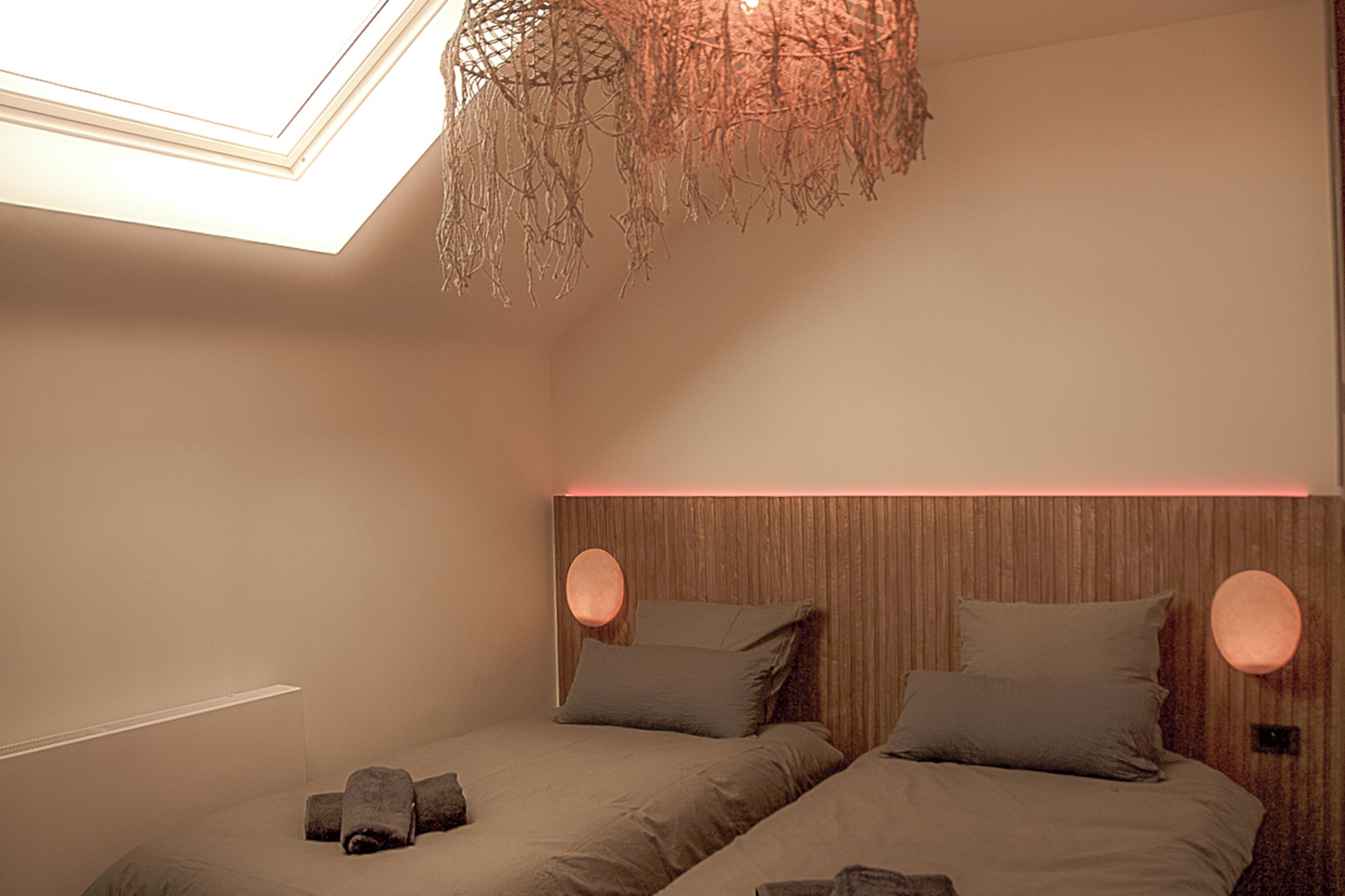 A bedroom with two beds, a skylight, and a hanging light fixture.