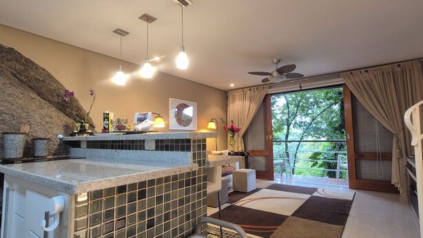 A modern kitchen with a stone backsplash, a dining area with a view, and a balcony with curtains.