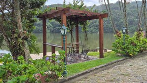 A gazebo with benches and tables, surrounded by lush greenery and a view of a lake.