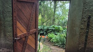 A rustic wooden gate with a metal latch, leading to a lush garden area with a stone pathway and a metal grate on the ground.