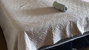 Un lit bien fait, avec une couverture matelassée, un oreiller et une serviette pliée posée dessus.