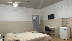 Une chambre avec deux lits, un bureau, une chaise, un réfrigérateur et un ventilateur de plafond.