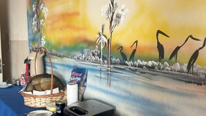 Une table de buffet avec divers plats, un tableau représentant des oiseaux et des arbres, et une machine à café.