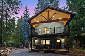 A two-story cabin with a balcony, surrounded by trees.