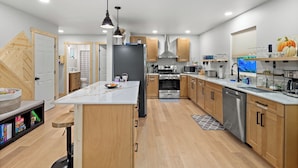 Una cocina moderna con armarios de madera, una isla central, electrodomésticos de acero inoxidable e iluminación colgante.