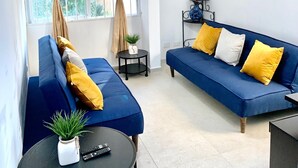 A living room with a blue sofa, a small round table with a plant and remotes, and a ceiling fan. - 2BR Apartment near Mamitas Beach (Playa del Carmen)
