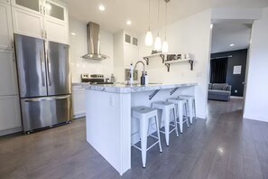 A modern kitchen with stainless steel appliances, a marble countertop, and a central island with bar stools. - Modern Townhouse in Signature Falls (Grande Prairie)
