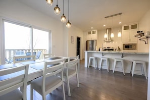 A modern kitchen with white cabinetry, a central island with stools, and pendant lighting. - Modern Townhouse in Signature Falls (Grande Prairie)