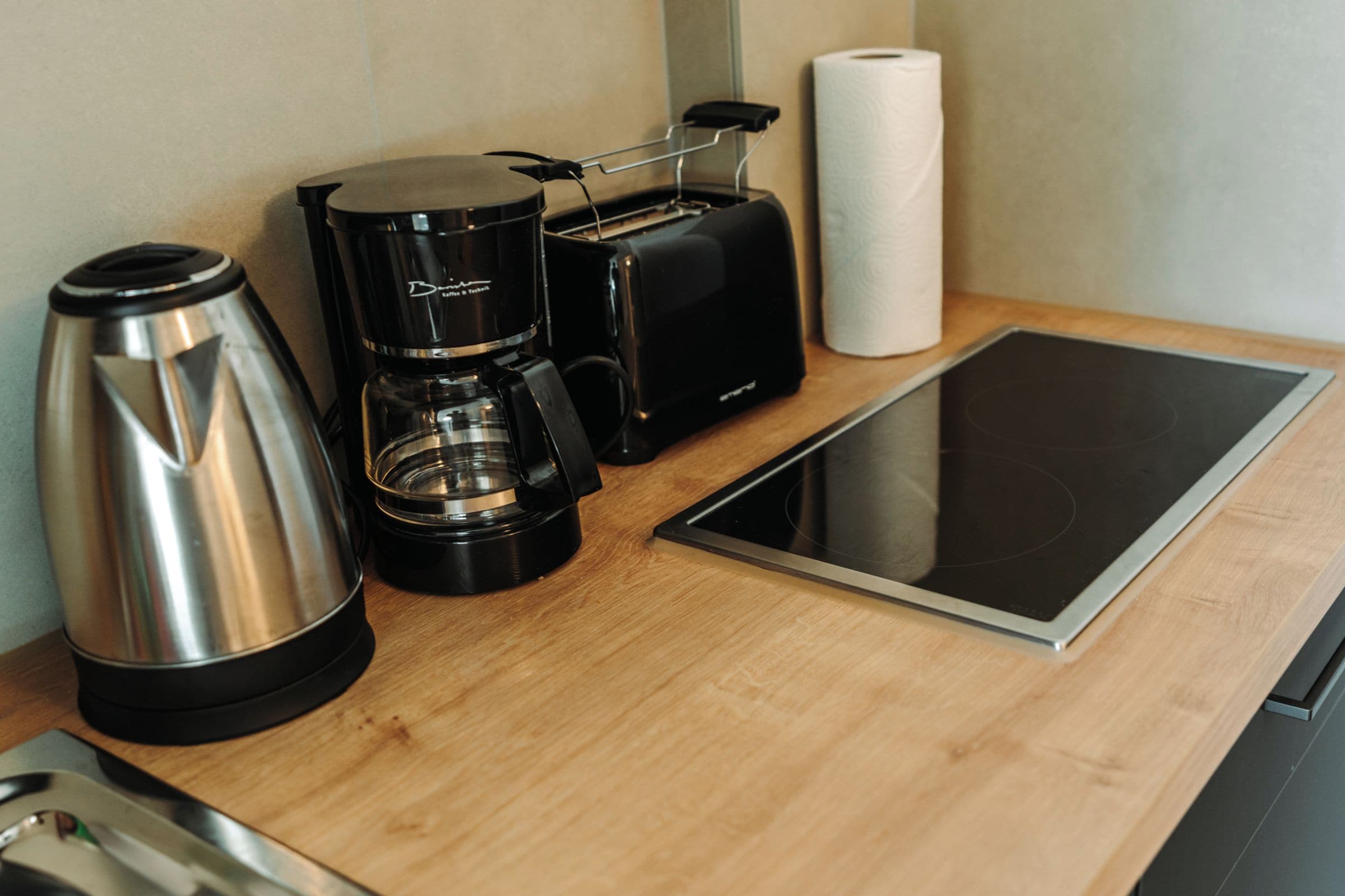 Eine Küchenzeile mit Kaffeemaschine, Toaster, Wasserkocher und einem Tablet auf einer Holzausziehtafel.