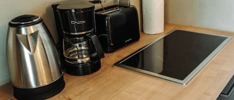 Una cocina americana con cafetera, tostadora, tetera y una tableta sobre una encimera de madera.