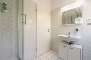 Une salle de bain moderne avec une douche à l’italienne en verre, un lavabo blanc avec un miroir au-dessus et un petit meuble en dessous.