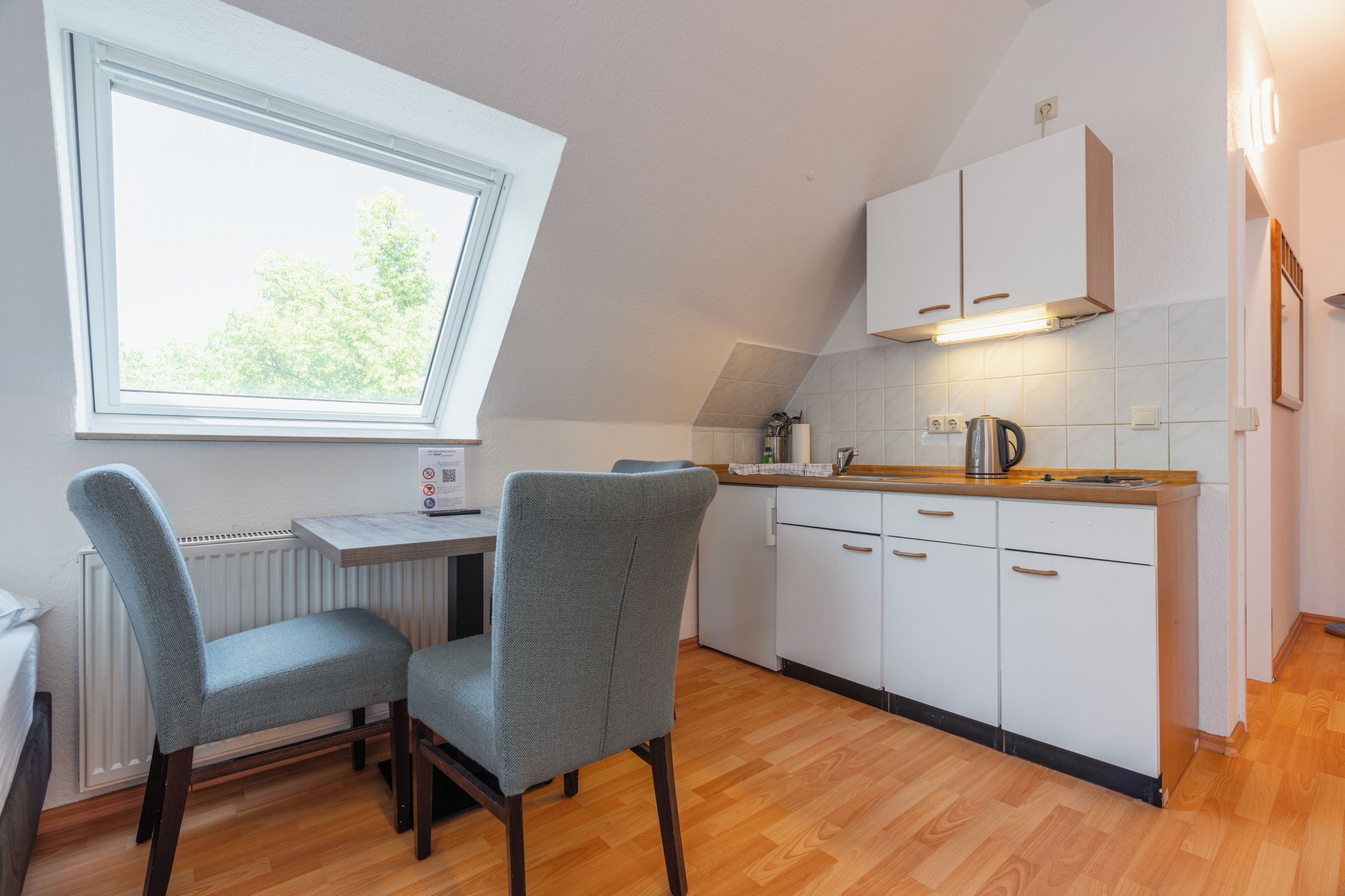 Une cuisine compacte avec un coin repas, dotée d’une fenêtre, de meubles blancs et d’un plan de travail en bois.