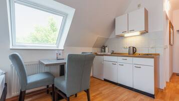 Une cuisine compacte avec un coin repas, dotée d’une fenêtre, de meubles blancs et d’un plan de travail en bois.
