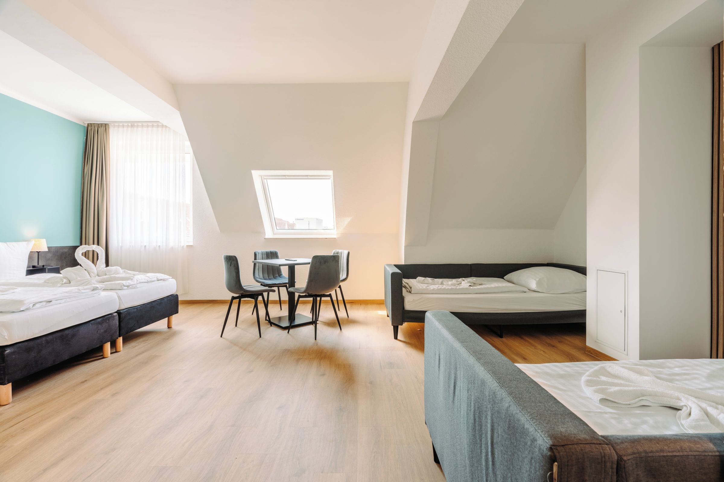 Quarto de hotel com duas camas, uma mesa de jantar com cadeiras, uma janela e vista para a paisagem urbana.